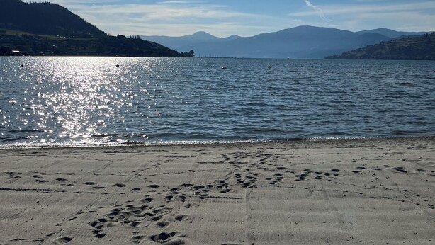 A beach with footprints in the sand, a clear sky, and mountains in the background. - Vernon Sandy Beachfront Home ! (Vernon)