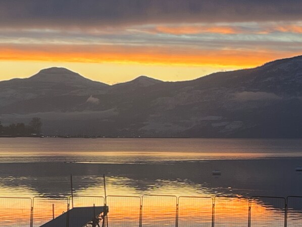 Atardecer sobre un lago con montañas al fondo y un muelle en primer plano.