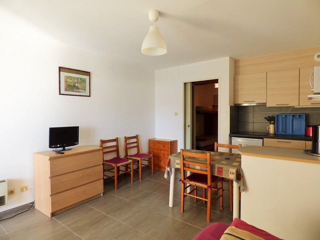 Un espacio habitable compacto con kitchenette, comedor y televisor sobre un aparador de madera.