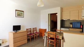 Un espacio habitable compacto con kitchenette, comedor y televisor sobre un aparador de madera.