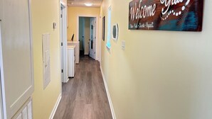 Un corridoio con un cartello che dice 'Welcome', un angolo lavanderia e una porta che dà su un'altra stanza.