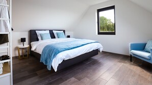 Une chambre à coucher avec un lit, une table de chevet, un canapé bleu et une fenêtre donnant sur des arbres.