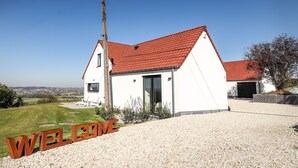 Une maison blanche avec un toit rouge, une allée en gravier et une pancarte indiquant « BIENVENUE ».