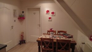 Een eethoek met een houten tafel en stoelen, een klein bijzettafeltje en een wandplank met een klok en een decoratie in de vorm van een hart.