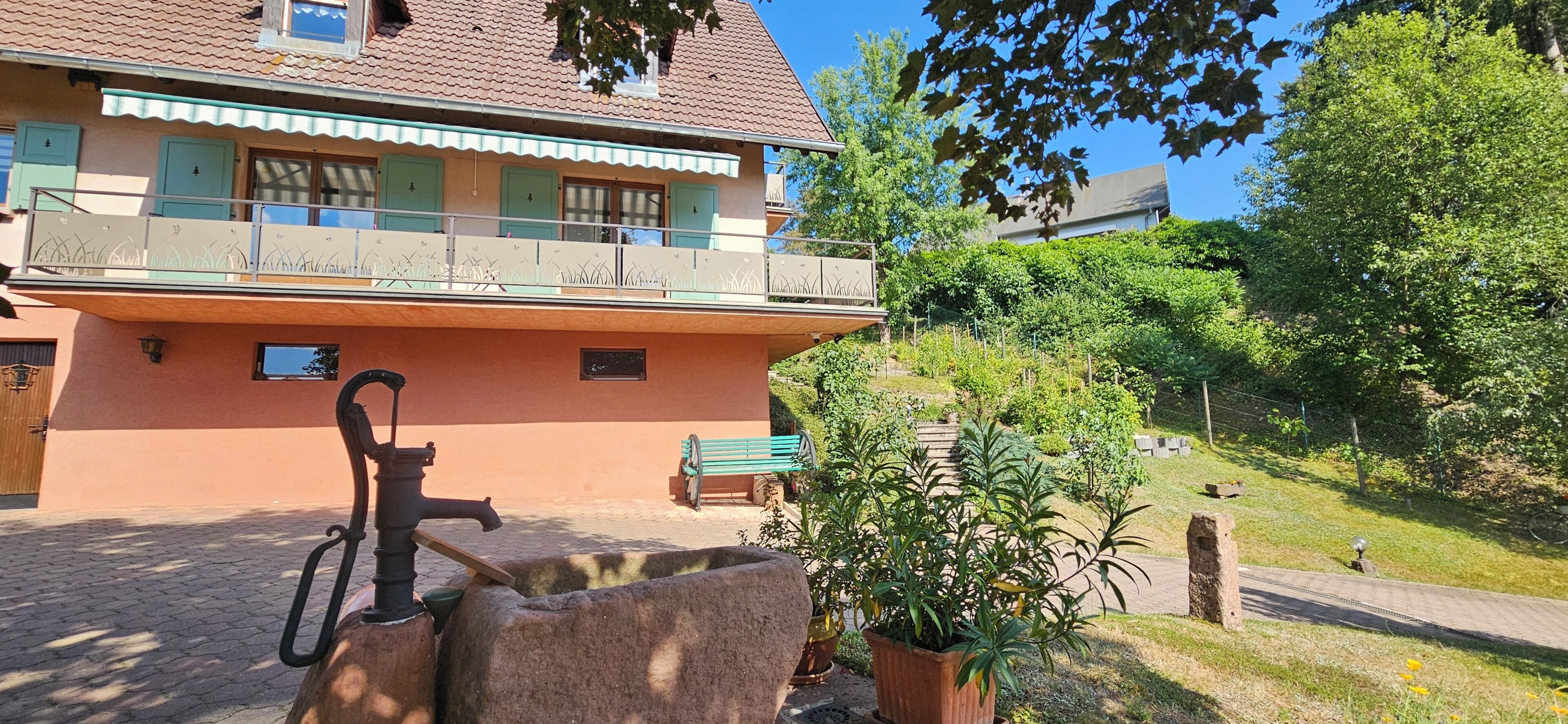 A two-story building with a balcony, a water spigot, and a pathway leading to a bench.