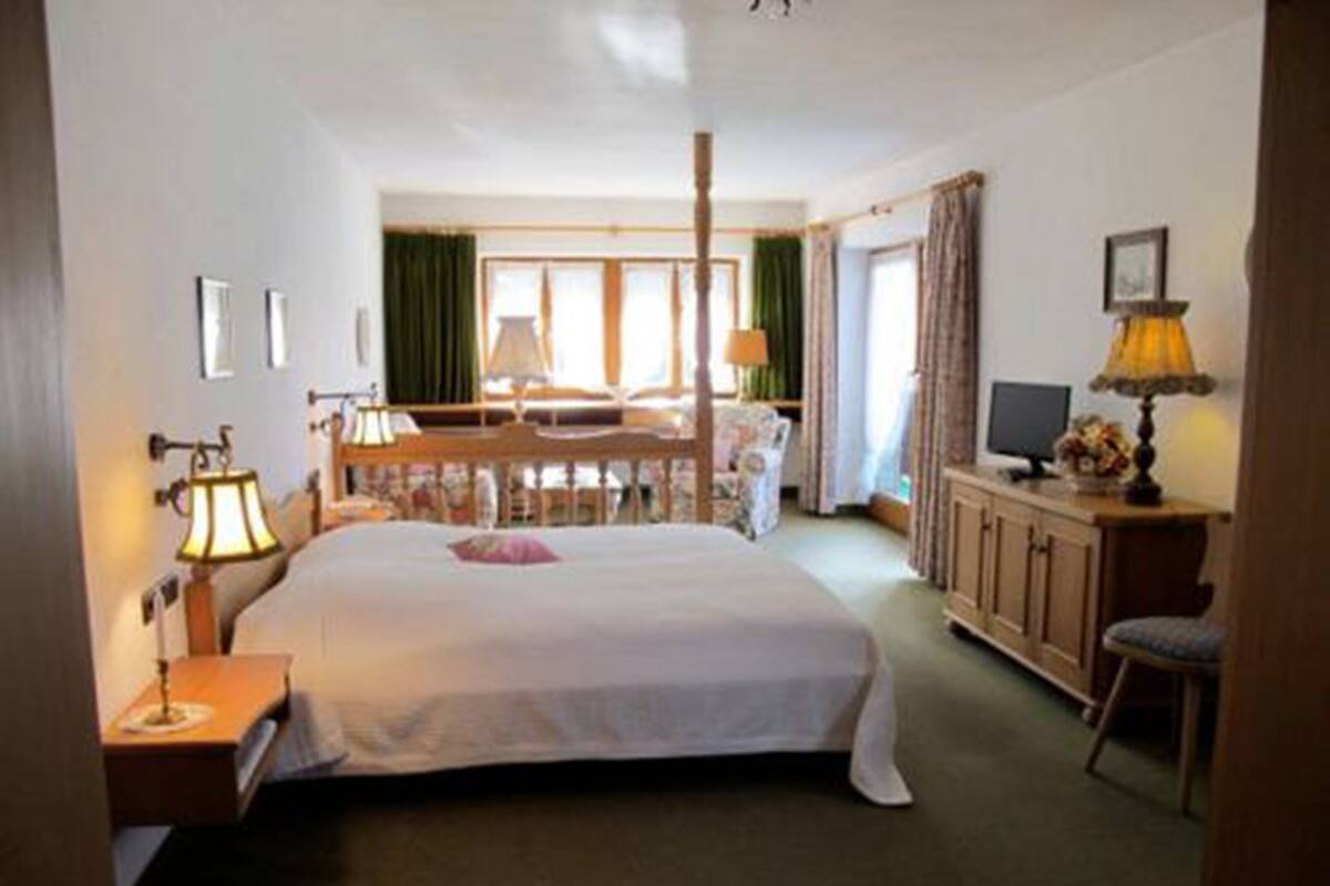 A hotel room with a large bed, a desk with a lamp, a chair, a television, and a window with curtains.