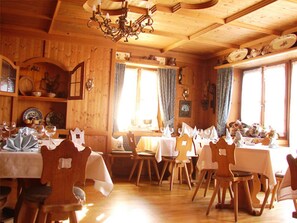 A wooden dining area with tables and chairs, a chandelier, and wooden walls. - Hotel & Restaurant Tonihof (Eschenlohe)
