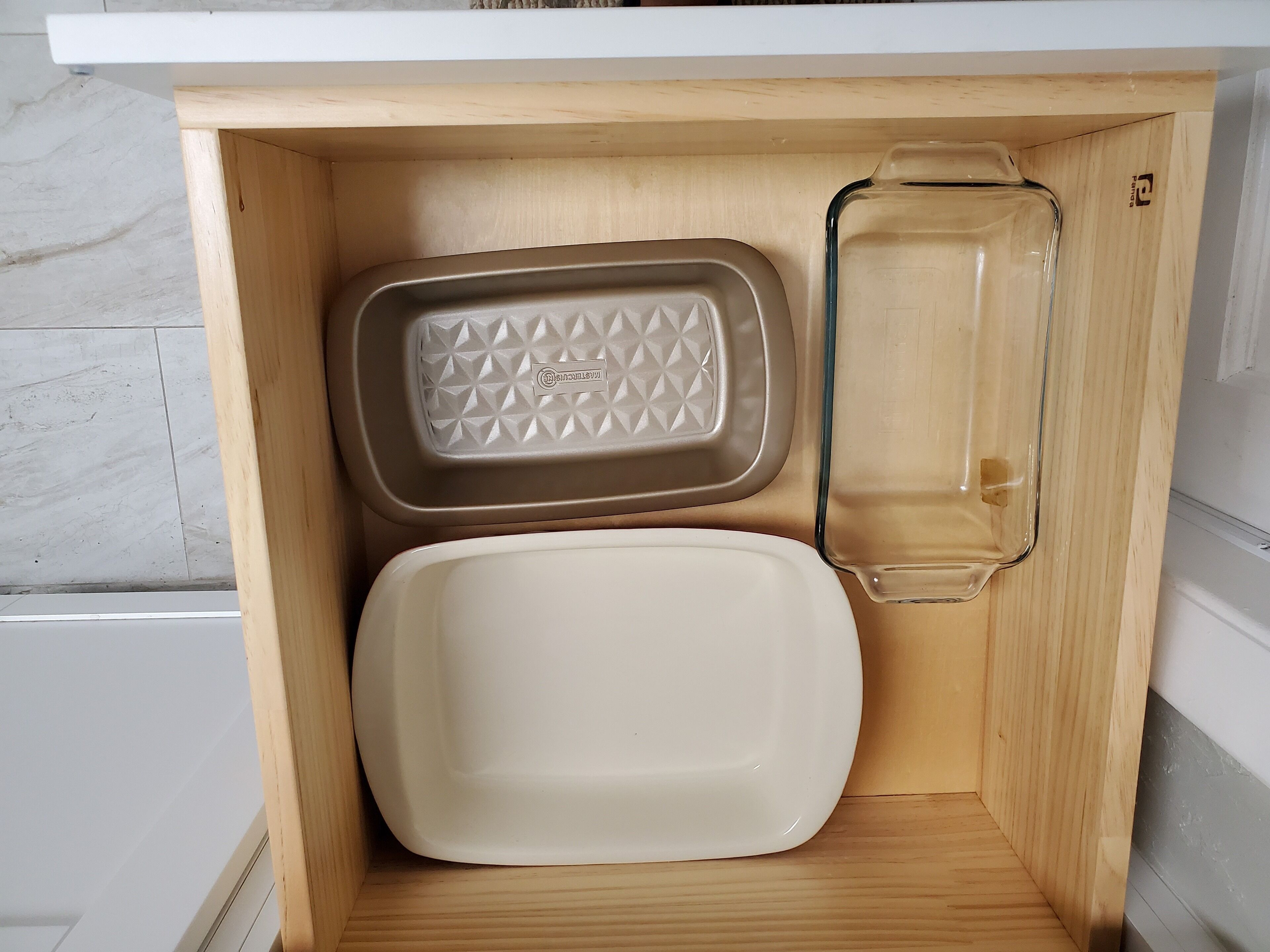 Un armario de cocina con encimera blanca, una bandeja para hornear color beige y un recipiente de vidrio transparente.