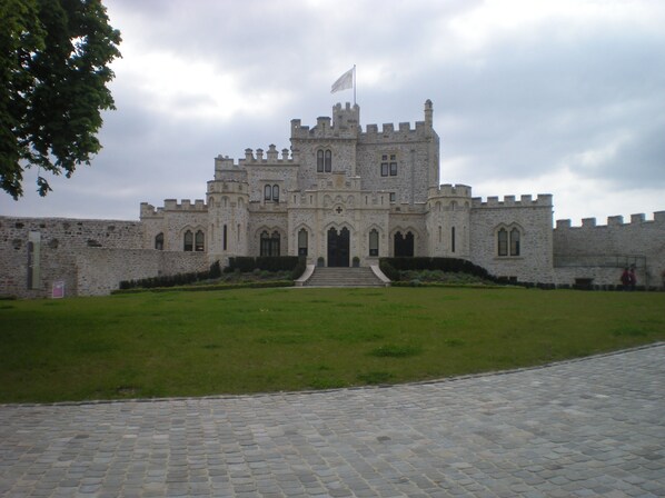 A large stone castle with a flag on top, a grassy courtyard, and a cobblestone pathway leading to the entrance. - Tourist apartment by the sea, Private parking, South facing balcony sea view (Camiers)