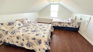 A small, triangular attic bedroom with two beds, a sloped ceiling, and a skylight. - Blue Water Villa B - Coastal Realty Group (Grand Isle)