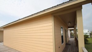 A single-story building with a covered porch and a wooden deck. - Blue Water Villa B - Coastal Realty Group (Grand Isle)