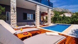 A modern outdoor pool area with lounge chairs and a stone pillar structure. - Luxury Villa Jasmina with heated pool by the sea!!! (Omis)