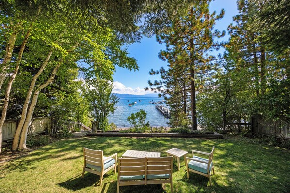 Patio con mobiliario de madera con vista a un lago con barcos y un muelle.