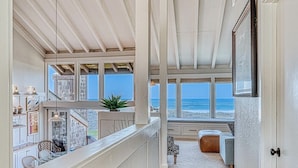 A spacious room with a view of the ocean, a balcony with outdoor seating, and a staircase leading to an upper level. - Oceanfront Retreat • Private Hot Tub • 3 King Suites + Loft • Walk to Beach (Castroville)