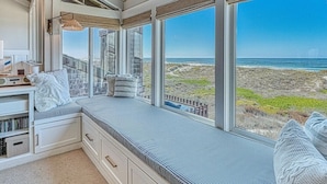 A room with a large window overlooking a beach, a built-in bench with cushions, and a bookshelf. - Oceanfront Retreat • Private Hot Tub • 3 King Suites + Loft • Walk to Beach (Castroville)