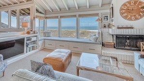 A spacious living room with a large window overlooking the beach, a fireplace, and a cozy seating area. - Oceanfront Retreat • Private Hot Tub • 3 King Suites + Loft • Walk to Beach (Castroville)