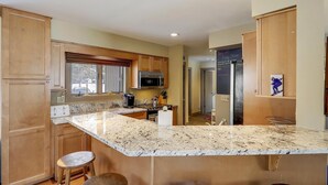 A kitchen with wooden cabinets, a granite countertop, and a stainless steel refrigerator. - Stowe Base Camp 21 at Stonybrook: 3 br, fireplace, a/c, decks, summer pool & community amenities! (Stowe)