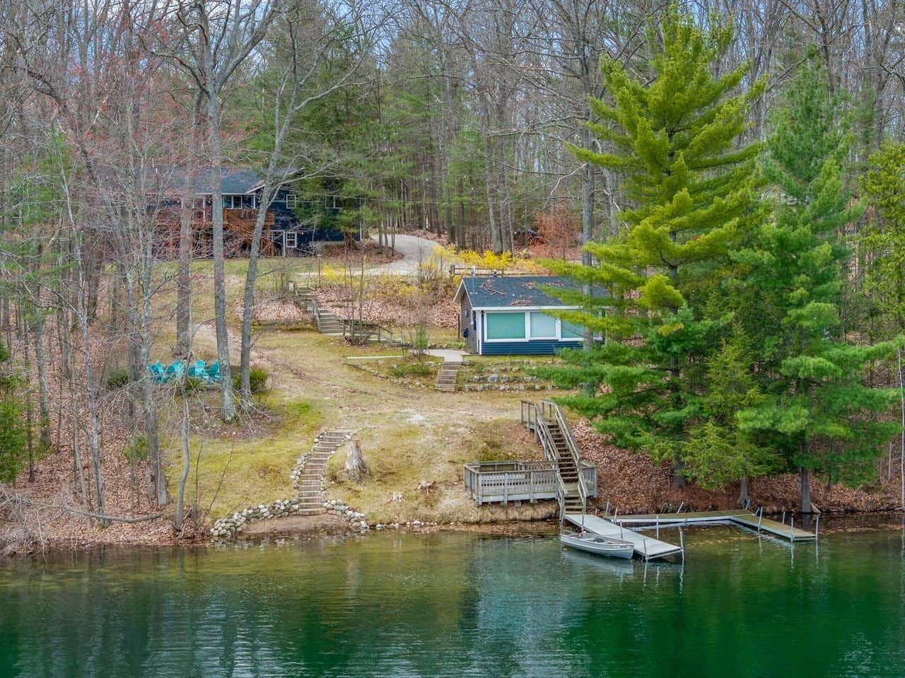 Un chalet au bord du lac, doté d’un quai, entouré d’arbres et accessible par un petit pont.
