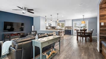 Una sala de estar moderna con un sofá seccional, una mesa de centro y un televisor. Se observa un comedor con una mesa y sillas. La cocina es visible al fondo, con una ventana que muestra una vista nevada.