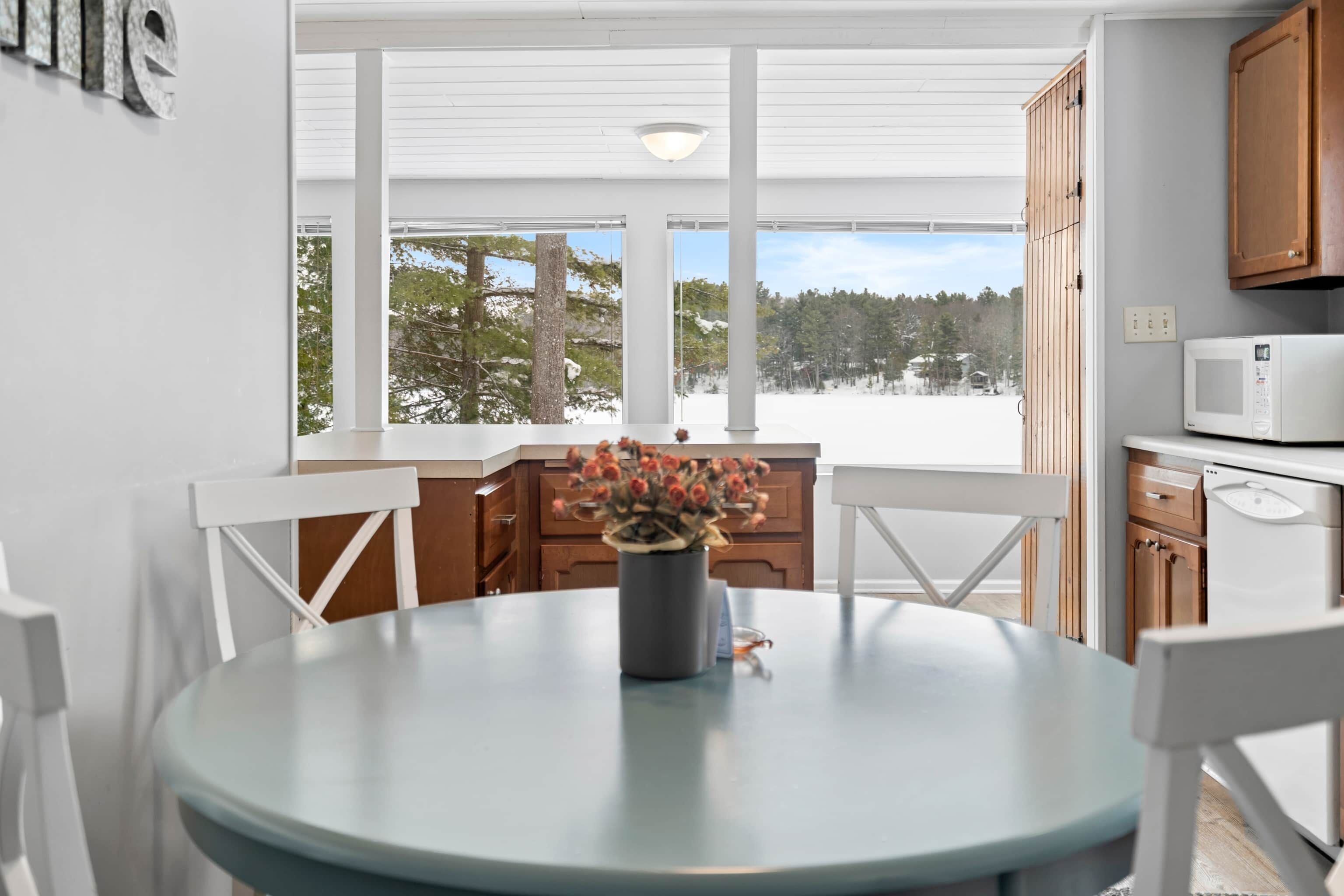 Une cuisine moderne avec des meubles blancs, une table ronde entourée de chaises et une vue sur un paysage enneigé grâce à de grandes fenêtres.