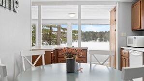 Moderni keittiö, jossa on valkoiset kaapit, pyöreä pöytä tuoleineen ja suuret ikkunat, joista avautuu näkymä lumiseen maisemaan.