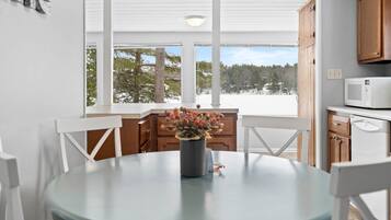 Una cocina moderna con armarios blancos, una mesa redonda con sillas y vistas a un paisaje nevado a través de ventanas amplias.