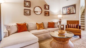 A living room with a beige sectional sofa, a round coffee table, and a staircase in the background. - Top Floor Spacious Ocean View Condo! Minutes to Beaches, A/C, Wifi, Pool (Kihei)