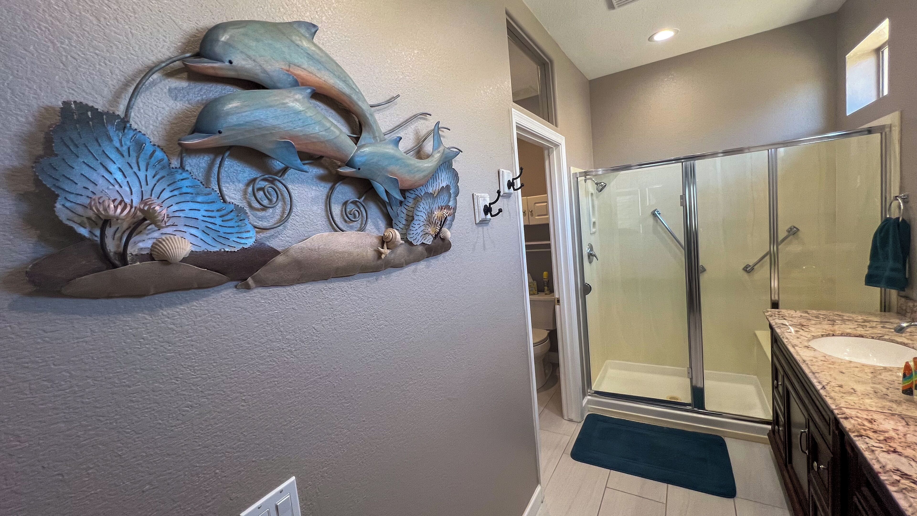 A bathroom with a glass shower enclosure, a marble sink, and a decorative wall piece with seashells and fish.