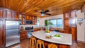 Una cocina con gabinetes de madera, un refrigerador de acero inoxidable, una isla grande con taburetes y un ventilador de techo.