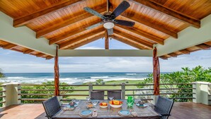 Un área de comedor al aire libre cubierta, con una mesa lista para dos, con vista al océano.
