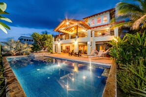 A two-story building with a swimming pool, outdoor seating, and tropical plants. - Oceanfront 5 Bedrooms with Amazing Pool, Great Ocean and Sunset Views! (Playa Negra)