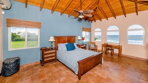 Un dormitorio con techo de madera, una cama, un escritorio y vista al océano.