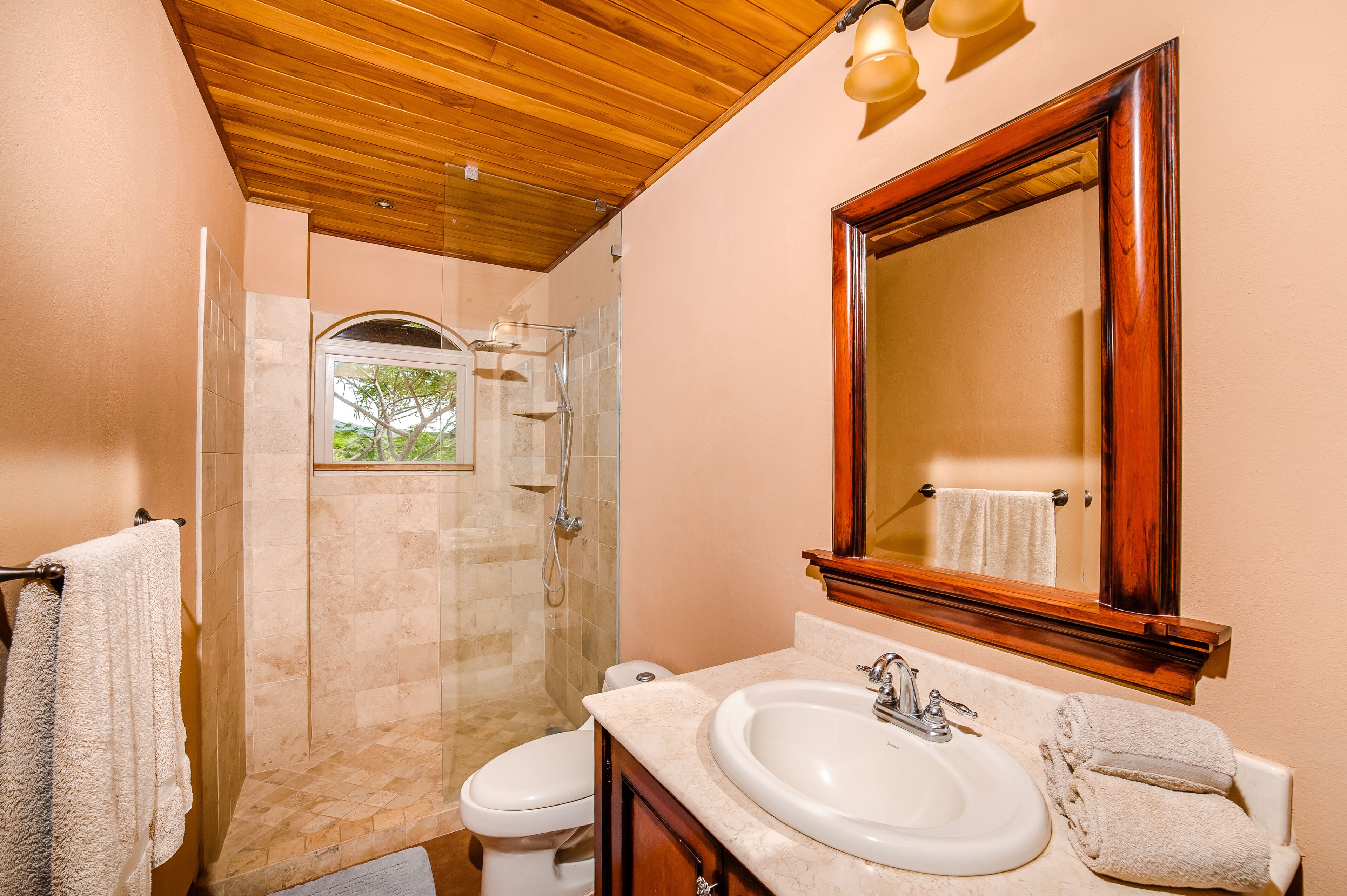 A bathroom with a wooden ceiling, a large mirror, a sink, and a shower.