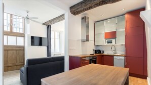 A modern kitchen with red cabinets, a wooden dining table, and a black sofa in a bright room with large windows. - Saint Paul, Marais History France Louis XIV &XV (Paris)