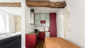 A compact kitchen with red cabinetry, a microwave, and a wooden dining table. - Saint Paul, Marais History France Louis XIV &XV (Paris)