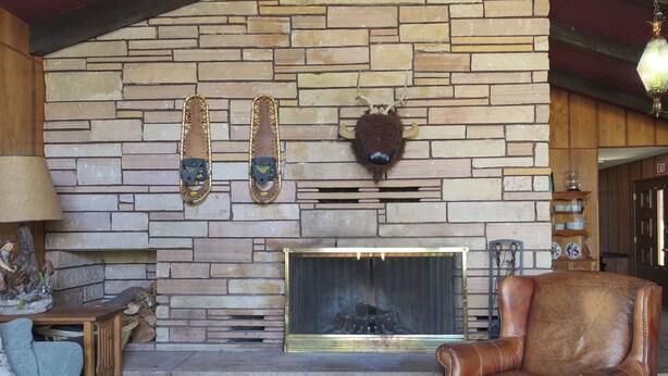 Una chimenea de piedra con leña encendida, un sillón de cuero y una cabeza de animal montada.