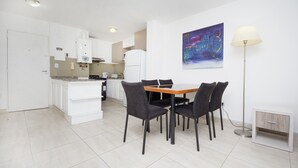 Cozinha moderna com armários brancos, mesa de jantar com cadeiras, um abajur e um quadro na parede.