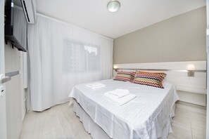 A hotel room with a large bed, white curtains, a headboard with lights, and a flat-screen TV mounted on the wall. - Buenos Aires Flat L8K (Córdoba)