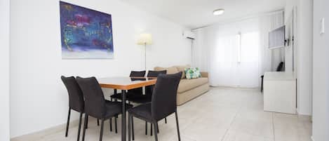 A modern living room with a dining table and chairs, a sofa, a TV, and a painting on the wall.