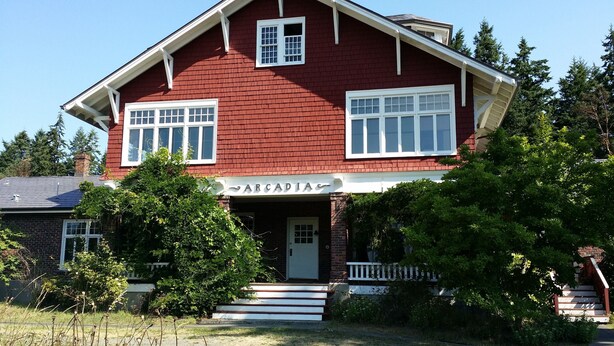 A two-story red brick house with a white front porch and a sign reading "ARCADIA".