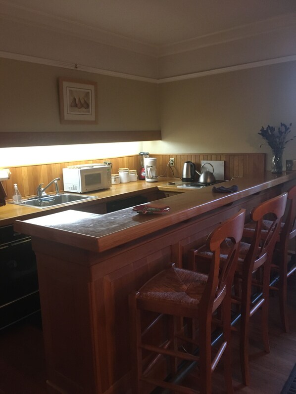 Una cucina con isola in legno, sgabelli da bar, forno a microonde, bollitore e macchina del caffè.