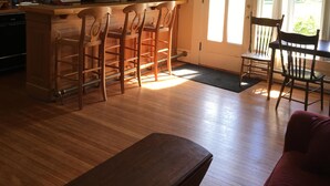 A spacious kitchen with wooden bar stools, a dining area with a red sofa, and a bench.