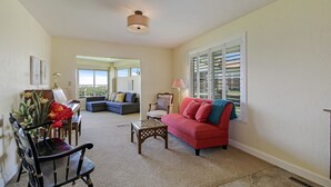 A living room with a piano, a red sofa, a coffee table, and a chair. There is a window with blinds and a lamp on a side table. - Panoramic Views overlooking the Colorado River Valley (Grand Junction)