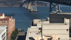Eine Hängebrücke mit mehreren Türmen und Kabeln, die über ein Gewässer führt, wobei sich im Vordergrund Gebäude befinden.