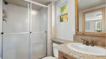 A bathroom with a glass shower enclosure, a white toilet, a granite countertop sink, and a wooden vanity.