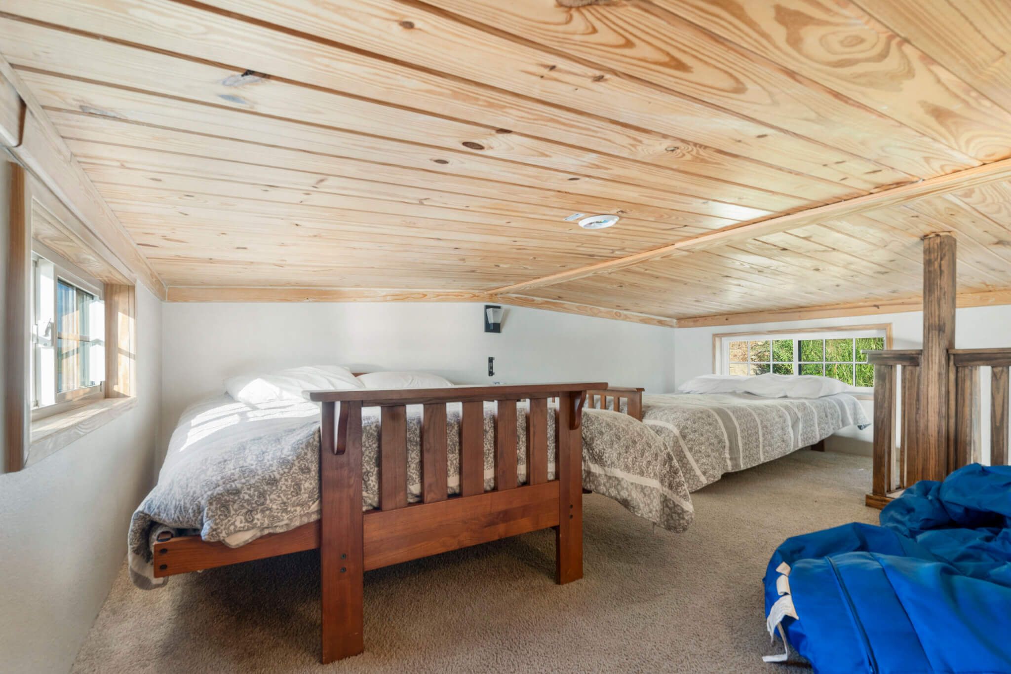 A bedroom with two wooden beds, a window, and a ceiling with wooden beams.