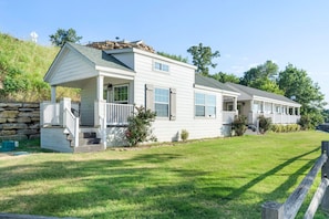 A two-story white house with a porch, a stone retaining wall, and a well-maintained lawn. - Fox Den at CrossTimbers Marina (Sperry)