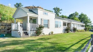A two-story white house with a porch, a stone retaining wall, and a well-maintained lawn. - Fox Den at CrossTimbers Marina (Sperry)