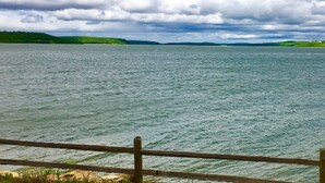 A lake with a wooden fence in the foreground and green hills in the background. - Fox Den at CrossTimbers Marina (Sperry)