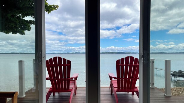 Blick aus einem Zimmer auf ein Gewässer, mit zwei roten Adirondack-Stühlen.